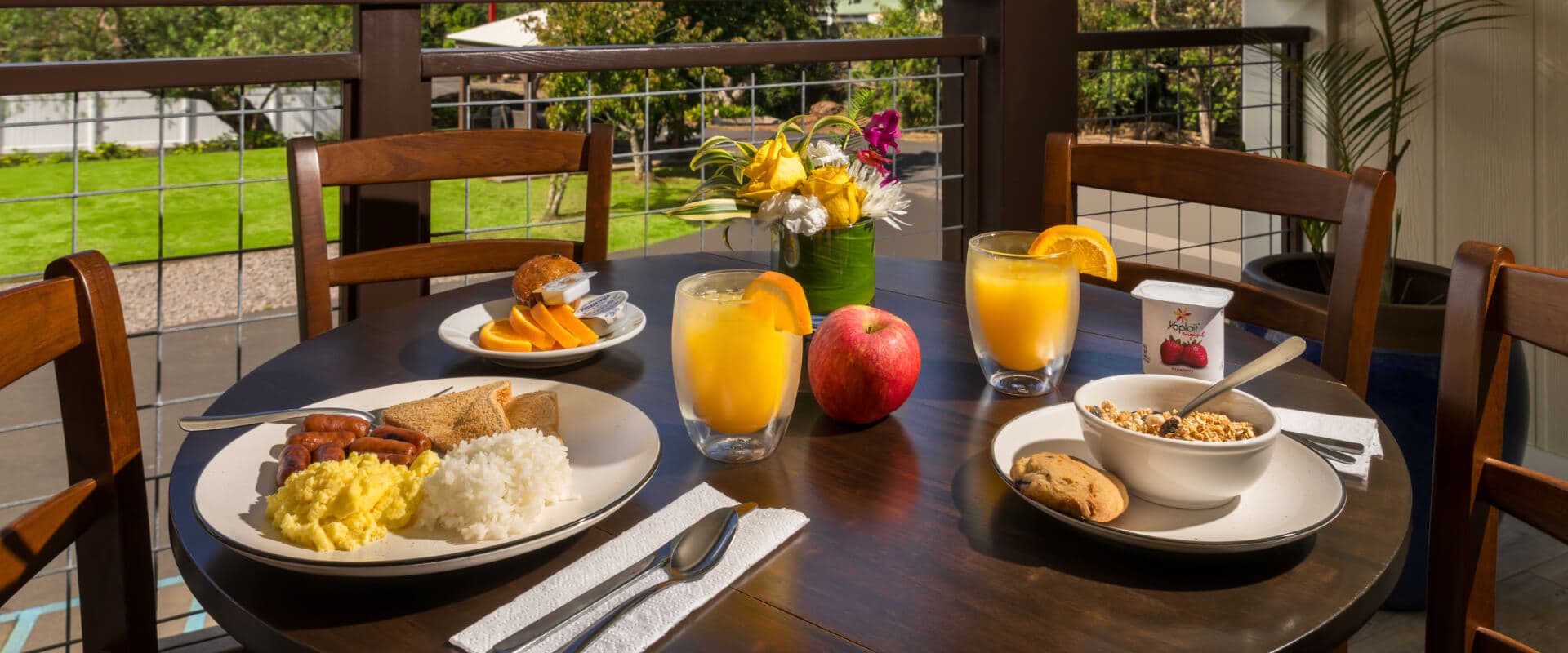 A dining table set with a breakfast spread including eggs, rice, sausage, fruit, juice, and pastries.