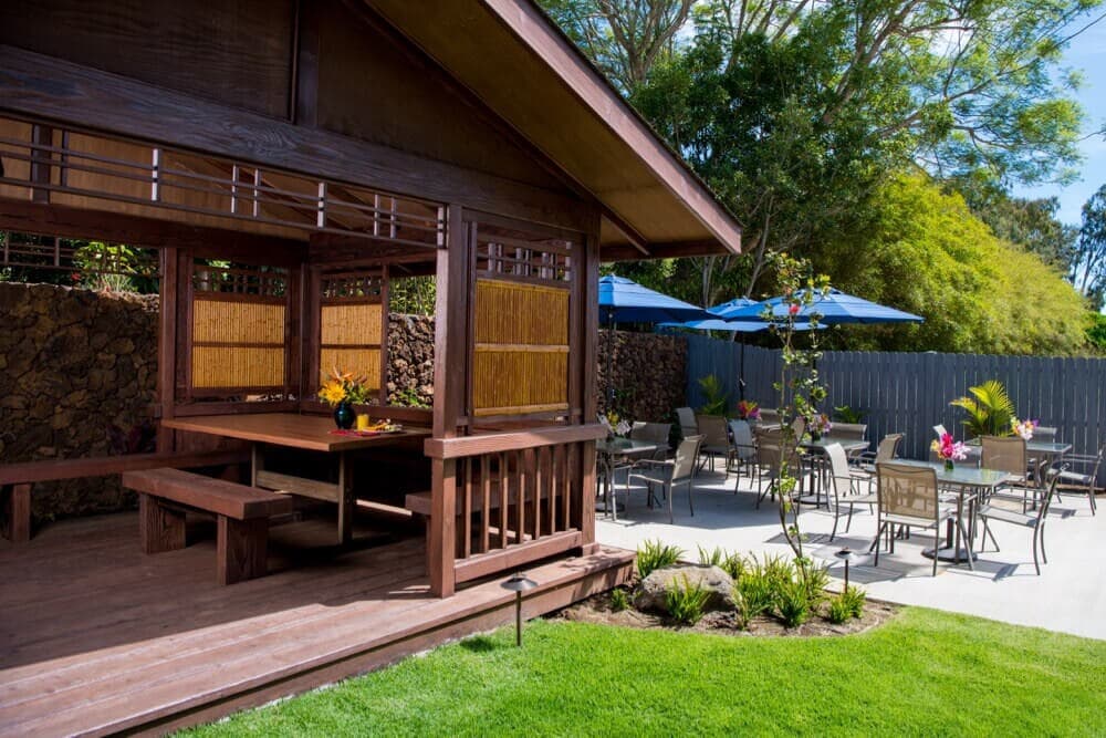 A wooden gazebo with seating surrounded by a patio and garden area.