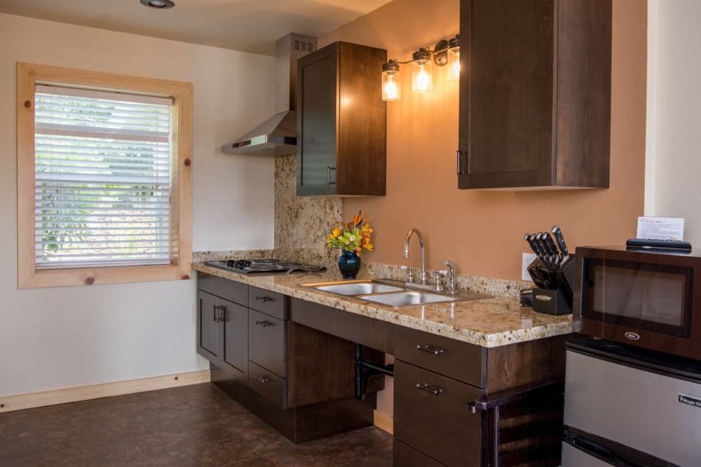 A modern kitchen featuring dark cabinets, a granite countertop, and a window with blinds.