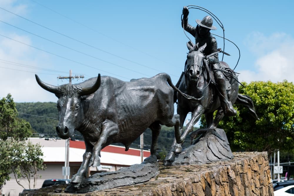 A bronze sculpture of a cowboy roping a bull atop a stone base.