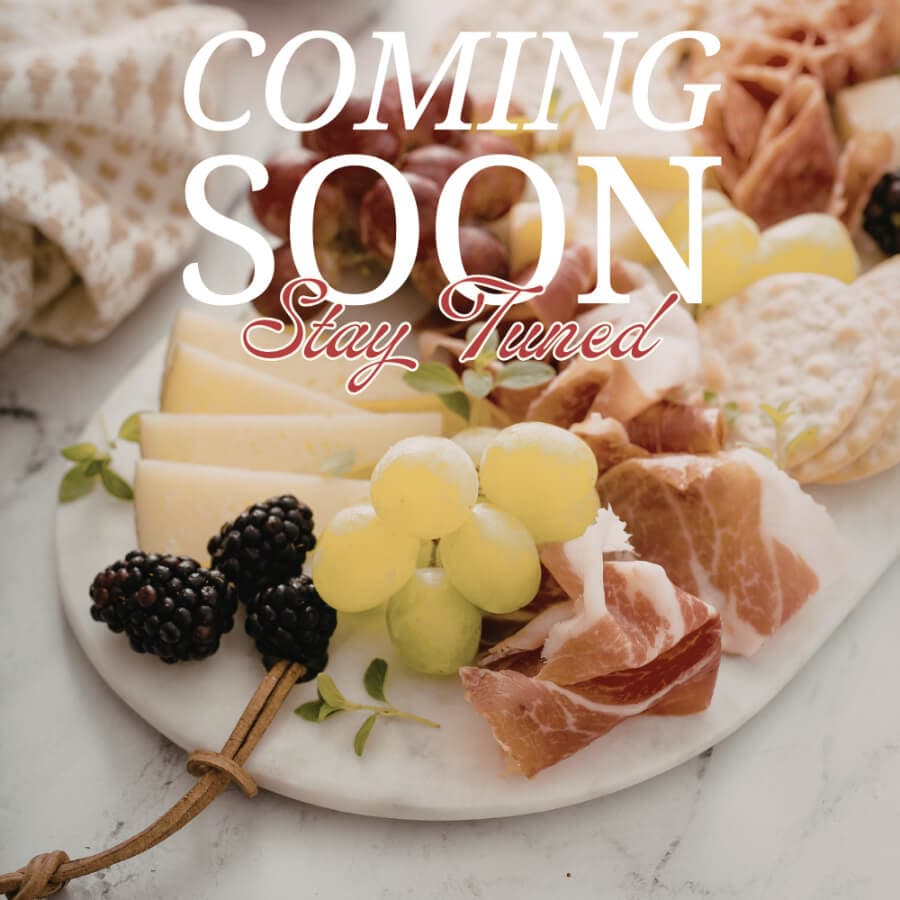 A charcuterie board featuring various cheeses, meats, and fruits with the text "COMING SOON Stay Tuned" overlayed.